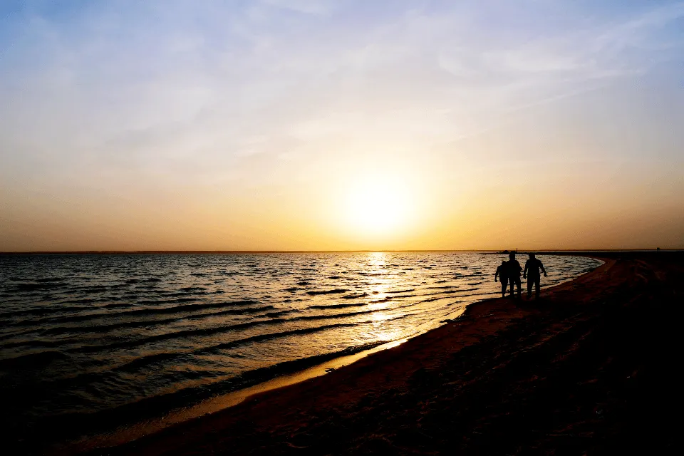 Two people walking along the beach at sunset, the kind of free memorial gathering many families hold after a basic cremation